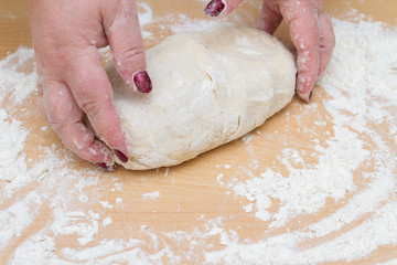 Kneading dough with flour on a wooden table at home