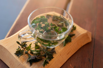 Cup of herbal tea with nettle on wooden background