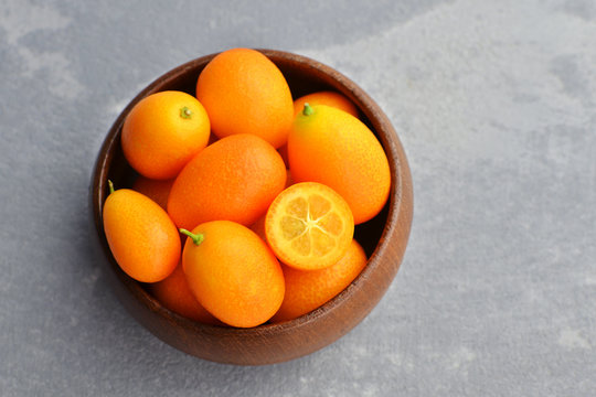 Fresh organic kumquat fruits in wooden bowl on concrete background. Healthy vegan food. Kumquat fruit cut in half. Top view. Copy space. © nikavera