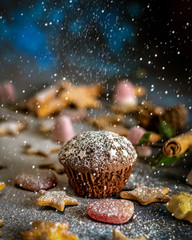 Cocoa muffins in a cloud of icing sugar surrounded by Christmas sweets