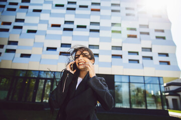 Young businesswoman speaking on mobile phone during outdoor coffee break, near office building. Communication concept