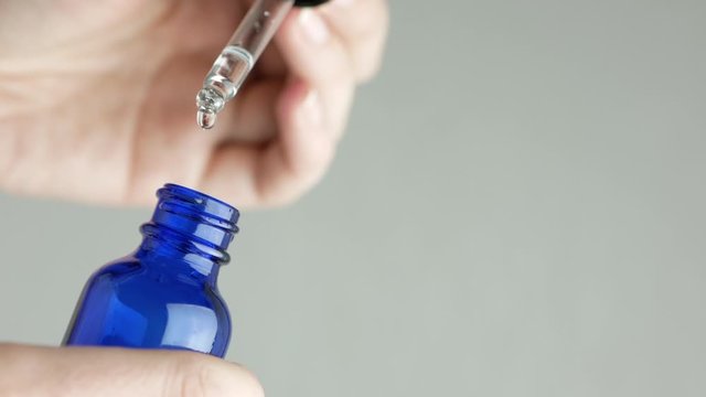 Woman&rsquo;s hand holding pipette. Close-up of dropper bottle pipette and cosmetic transparent oil