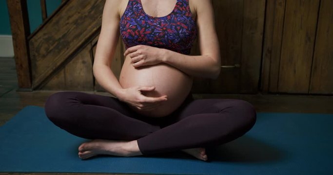 Pregnant young yoga woman feeling her belly before meditating