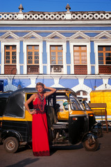 girl in the  of the Indian city in, a red dress posing on the background of an auto rickshaw.
