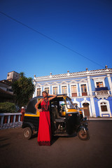 girl in the  of the Indian city in, a red dress posing on the background of an auto rickshaw.