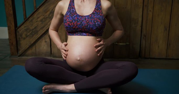 Pregnant young woman on yoga mat feeling her belly