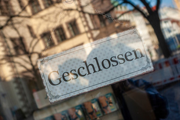 Schaufenster von Ladengeschäft mit Schild „Geschlossen“, in Deutsch, mit Auslagen und die Spiegelung der Umgebung in Unschärfe zur Zeit der Corona Covid-19 Pandemie im März 2020