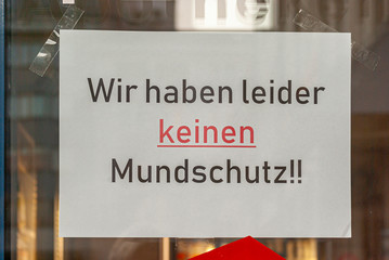 Schaufenster von Ladengeschäft mit Schild „Wir haben keinen Mundschutz“, in Deutsch, mit Auslagen und die Spiegelung der Umgebung in Unschärfe zur Zeit der Corona Covid-19 Pandemie im März 2020