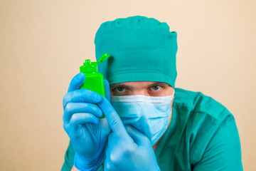 Green antiseptic bottle in Doctor hands in green suit and blue mask gloves with on yellow background. It is important to use antiseptic on your hands 