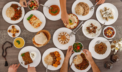 Iftar. Arabic family dinner after fasting. People sharing plates by hands. Ramadan Kareem, Eid Mubarak. Top view of table with food. Lebanese cuisine. Muslim people.