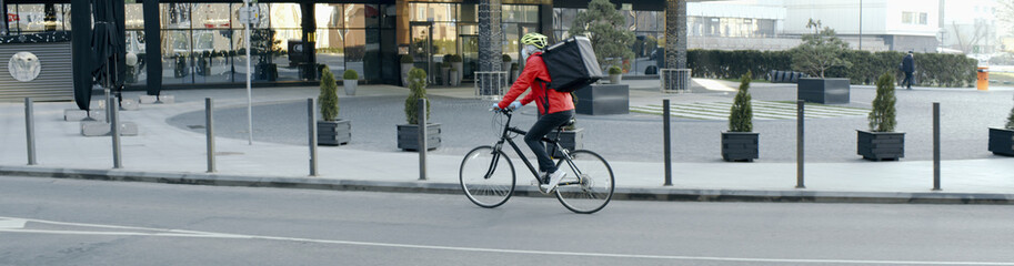 Fototapeta na wymiar Courier wearing medical mask and gloves riding a bicycle to deliver food order to customers during virus outbreak. Coronavirus, COVID-19, safe delivery