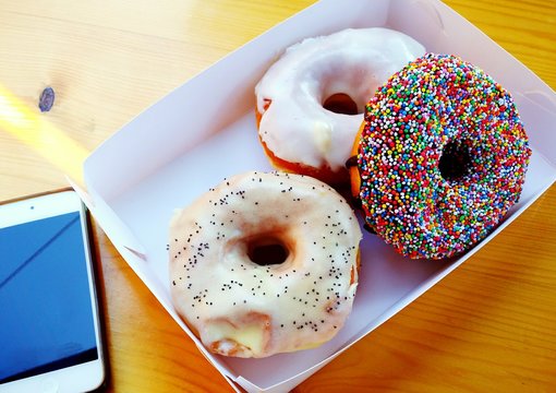 High Angle View Of Fresh Donuts In Box By Mobile Phone On Table