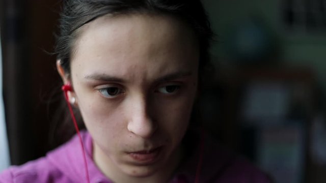 Young caucasian girl in pink sweater at computer with red headphones and concerned look on her face