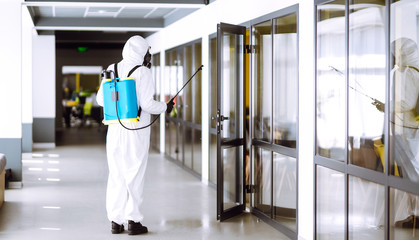 Disinfecting of office to prevent COVID-19, Man in protective hazmat suit with  with spray...