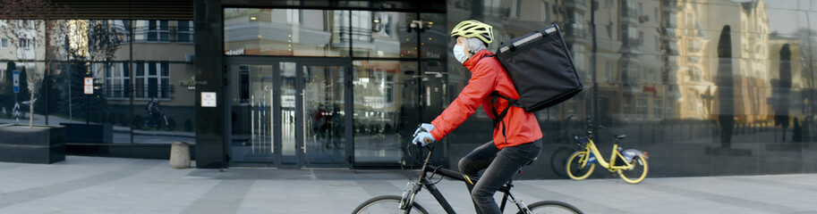 Courier wearing medical mask and gloves riding a bicycle to deliver food order to customers during virus outbreak. Coronavirus, COVID-19, safe delivery