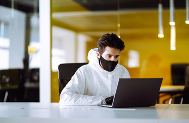 Man in protective hazmat suit and mask works on a computer in an empty office. Concepts to preventing the spread of coronavirus, pandemic in quarantine city. Covid -19.