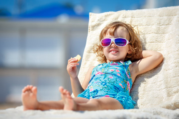 Adorable little girl enjoying on a sun lounger rest on the beach chair on tropical sandy beach sea shore. Sunbathing and leisure on sunny day. Travel with young children