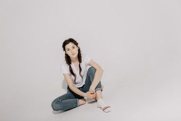 Young pretty woman with pigtail braid dressed in white t-shirt and jeans posing for photo on a white background in front of studio light