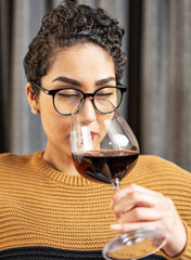 A woman wearing glasses and a sweater smelling red wine    