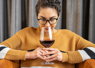 A woman wearing glasses and a sweater smelling red wine    