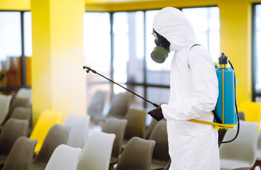 Man wearing protective suit disinfecting assembly hall with spray chemicals to preventing the spread of coronavirus, pandemic in quarantine city. Disinfecting of office. COVID-19.