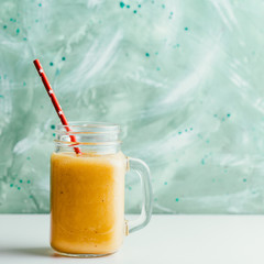 Ripe mango smoothie in a jar on a green background
