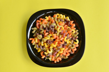 A plateful of colorful fusilli macaroni, on yellow background. 