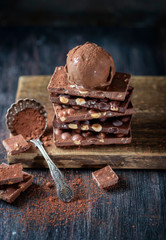 A ball of chocolate ice cream on a chocolate bar with nuts.