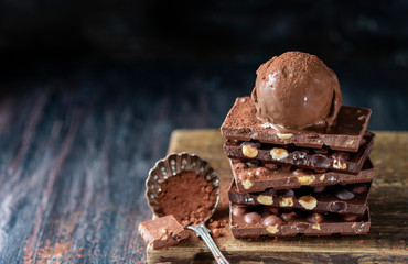 A ball of chocolate ice cream on a chocolate bar with nuts.