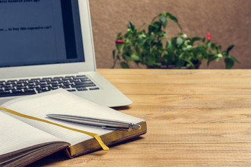 Pen on notebook and laptop on wood table.