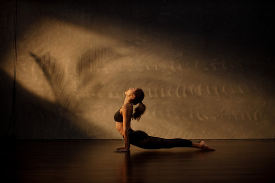Young Asian woman practicing yoga in moody studio during golden hour