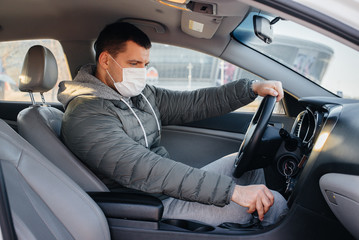 A young man sits behind the wheel wearing a mask for personal safety while driving during a pandemic and coronavirus. Epidemic