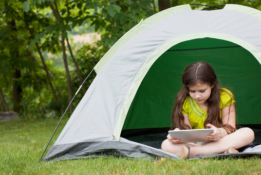 Candid image of girl in little tent in backyard working on tablet 