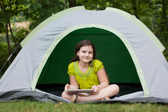 Portrait of girl in little tent in backyard working on tablet 