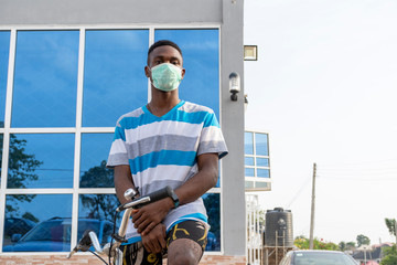 young black man on a bicycle outdoor wearing a face mask to protect against the coronavirus