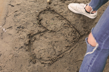 Herz im nassen Sand zwischen den Füßen einer jungen Frau. Standort: Deutschland, Nordrhein Westfalen