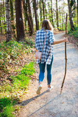 Junge Frau wandert durch den Wald. In der Hand hält sie einen Wanderstock. Ansicht von Hinten bei Gegenlicht. Standort: Deutschland, Nordrhein Westfalen