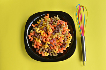 A plateful of colorful fusilli macaroni with whisk for whipping  on yellow background. 
