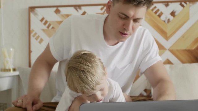 Close up of cute little kid son and adult dad learning to type on notebook
