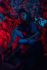 haute couture with pink blue neon hair. Young beautiful woman model, fashionable glowing hairstyle, makeup. Stylish Art Studio Portrait. Colorful Bright Light. black coat, newspaper background