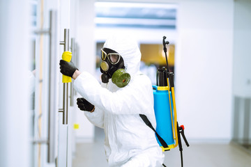 Man in protective hazmat suit washes door handles in office to preventing the spread of coronavirus, pandemic in quarantine city. Cleaning and disinfection of office. Covid-19.