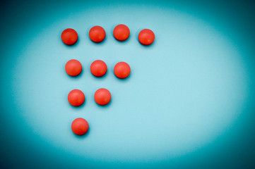 Red round medical pharmaceutical drug pills lie in the shape of a triangle or arrow on a blue background