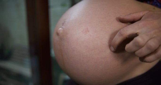 Pregnant young woman by window tapping and touching her belly