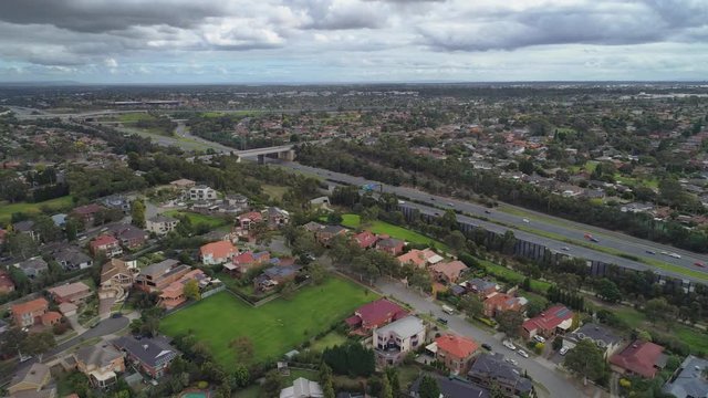 Aerial pan across suburban area and cars driving on highway in Melbourne, Australia