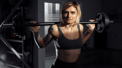 Fototapeta na wymiar Young sporty blonde woman doing heavy barbell exercise in fitness class.