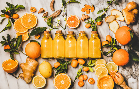 Immune boosting vitamin health defending drink. Flat-lay of fresh turmeric, ginger, citrus juice shot in glass bottles over marble background, top view. Vegan Immunity system booster