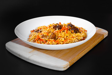 The concept of Oriental cuisine. National Uzbek pilaf with lamb meat in a white plate on a black background. Popular traditional dish of Eastern cuisine