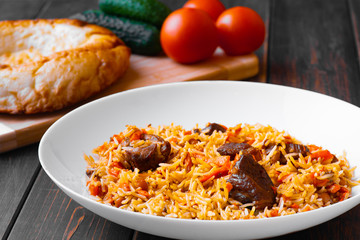 Traditional Uzbek, Iranian, Turkish, Azerbaijani, Indian, pilaf with lamb or beef meat on a wooden table with cucumbers and tomatoes. The concept of Oriental cuisine.