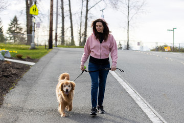 Woman walking her golden retriever dog outside for exercise and fresh air