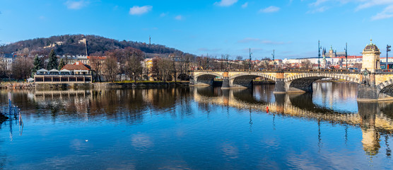 Fototapeta premium Legion Bridge, Czech: Most legii, reflected in Vltava River with Prague Castle and Petrin Hill on background. Clear sunny winter day in Prague, Czech Republic